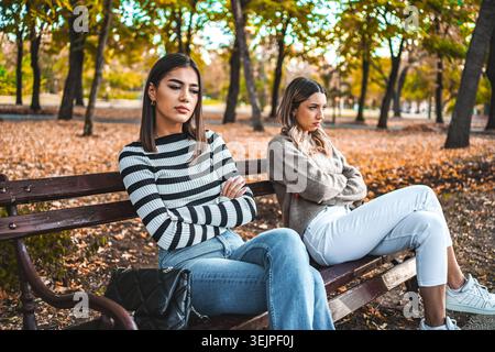 Due donne si siedono separate su una panchina del parco, arrabbiate l'una con l'altra Foto Stock