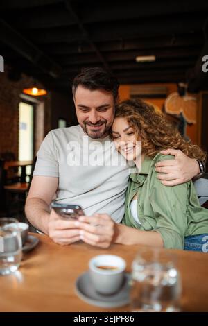 Coppia che guarda lo smartphone e sorride al bar Foto Stock