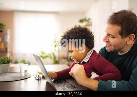 Padre che abbraccia figlio mentre impara con un portatile a casa Foto Stock