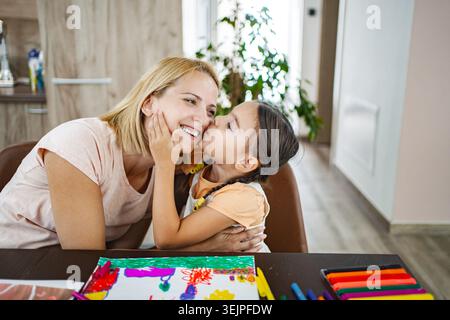 Madre e figlia condividono un momento di amore mentre creano arte a casa in una stanza accogliente e soleggiata Foto Stock