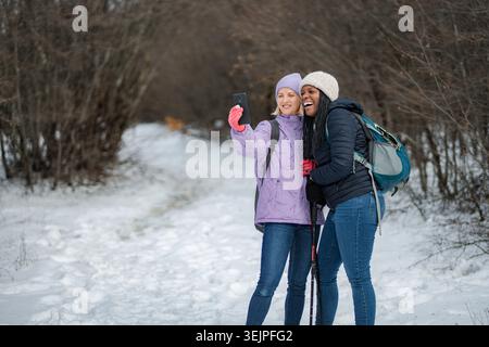 Felice giovane donna adulta amici che fanno trekking scattando selfie in inverno Foto Stock