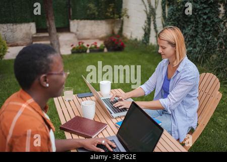 Due colleghi donne che lavorano all'aperto con notebook in giardino Foto Stock
