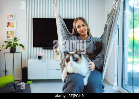 Adolescente che si rilassa in un'amaca con gatto ragdoll a casa Foto Stock