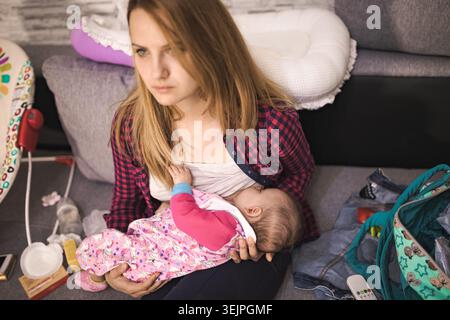 Mamma che allatta il bambino a casa in un salotto accogliente Foto Stock
