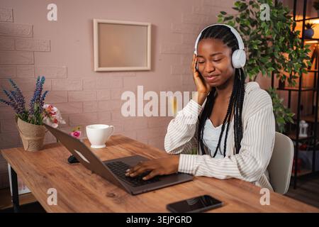 Giovane donna che ama la musica mentre lavora con un notebook a casa Foto Stock