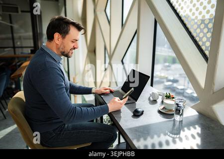 Uomo adulto maturo che lavora su computer portatile e smartphone Foto Stock