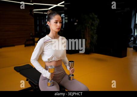 Donna che tiene i manubri mentre si fa esercizio in palestra Foto Stock