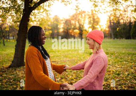 Diverse donne e amiche ridono tenendosi per mano nel parco Foto Stock