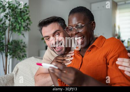 Felice coppia interrazziale che guarda il risultato positivo del test di gravidanza Foto Stock