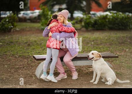 Madre e figlia abbracciano nel parco con il cane Foto Stock