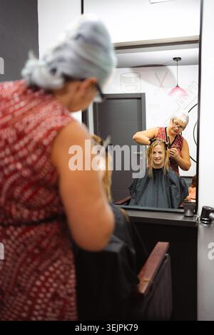 Parrucchiere che taglia i capelli bagnati della donna in un salone riflesso a specchio Foto Stock