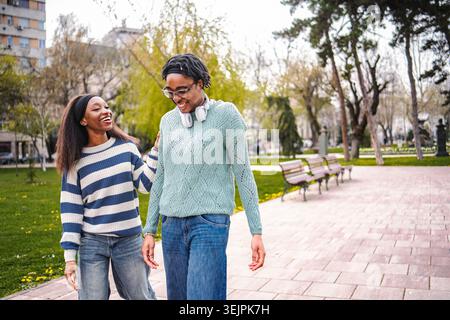 Due giovani amiche che ridono camminando nel parco Foto Stock