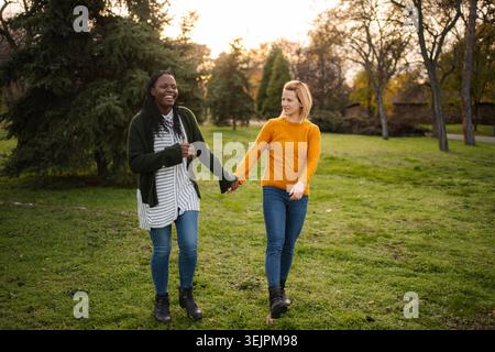 Diverse donne e amici camminano mano nella mano all'aperto ridendo Foto Stock