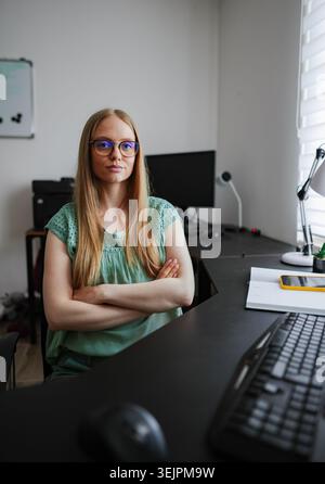 Donna sicura di sé seduta alla scrivania in un moderno spazio di lavoro dotato di tecnologia Foto Stock