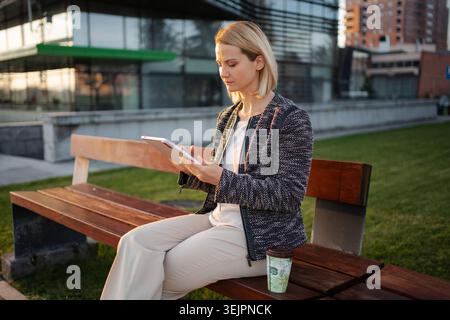 Donna d'affari che lavora su un tablet all'aperto per una pausa caffè Foto Stock