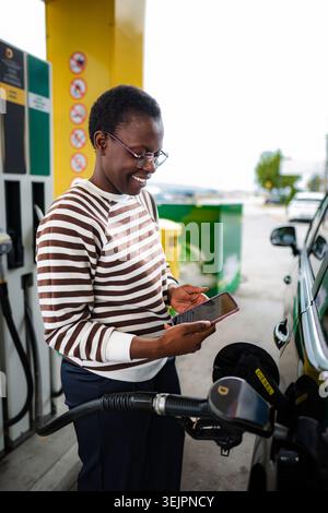Donna che rifornisce l'auto con diesel utilizzando lo smartphone per il pagamento Foto Stock
