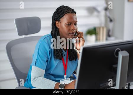 Infermiera che parla al telefono e usa il computer in ufficio medico Foto Stock