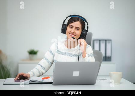 Donna che indossa un auricolare che lavora a distanza in un ufficio domestico Foto Stock