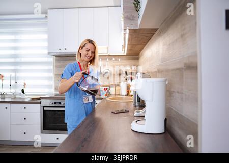 Infermiere che versa il caffè in una tazza in cucina durante una pausa Foto Stock