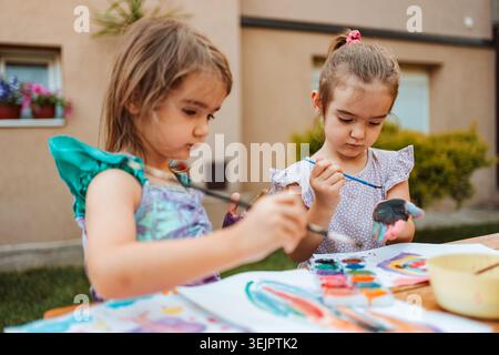 Due ragazze in età prescolare che dipingono con acquerelli nel cortile posteriore Foto Stock