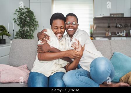 Due donne afroamericane si stanno abbracciando sul divano a casa Foto Stock