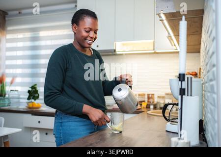 Donna che versa acqua calda per preparare tè al limone in cucina Foto Stock