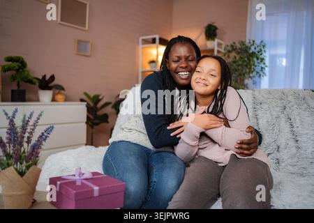 Madre felice che abbraccia figlia con una scatola regalo sul divano Foto Stock