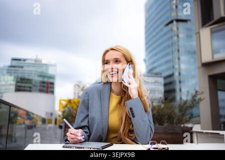 Donna d'affari che parla al telefono e lavora in remoto all'aperto Foto Stock