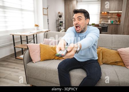 Uomo seduto sul lettino che tiene il telecomando Foto Stock