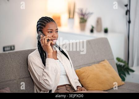 Giovane donna che parla al telefono mentre si rilassa sul divano Foto Stock