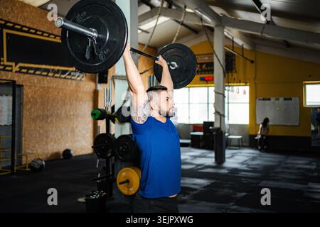Atleta maschile che solleva un pesante barbell che spinge in alto in palestra Foto Stock