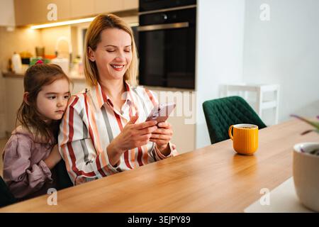 Madre che ignora il bambino mentre scorri i social media al telefono Foto Stock