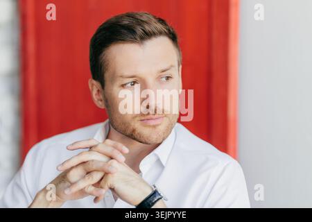 Ritratto di un uomo d'affari attento con le mani strette su sfondo rosso per un primo piano professionale Foto Stock