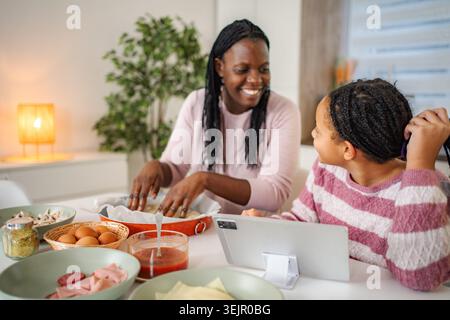 Mamma e figlia cucinano la pizza utilizzando un tablet digitale a casa Foto Stock
