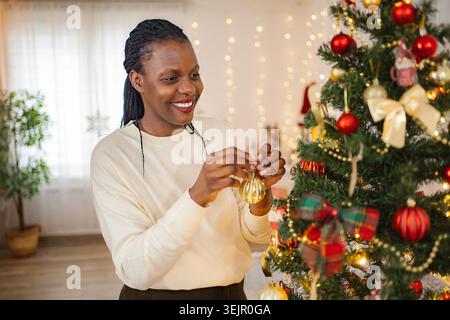 Donna sorridente mentre decora l'albero di Natale per le festività natalizie Foto Stock