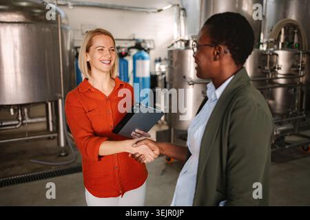 Donne d'affari che stringono la mano in una fabbrica di birra industriale Foto Stock