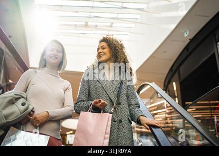 Due donne felici si divertono a fare shopping sulla scala mobile del centro commerciale Foto Stock