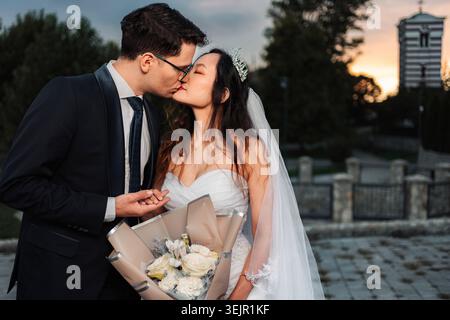 Matrimonio interrazziale che si baciano durante il romantico tramonto Foto Stock