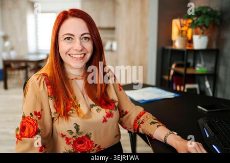 Ritratto di una donna sorridente dai capelli rossi a una scrivania Foto Stock
