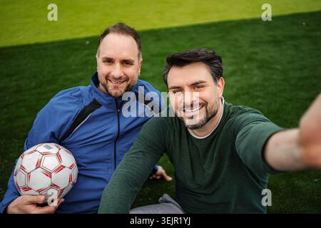 Due uomini sorridenti che fanno selfie sul campo da calcio Foto Stock