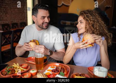 Coppia felice che mangia hamburger e beve birra in un ristorante Foto Stock