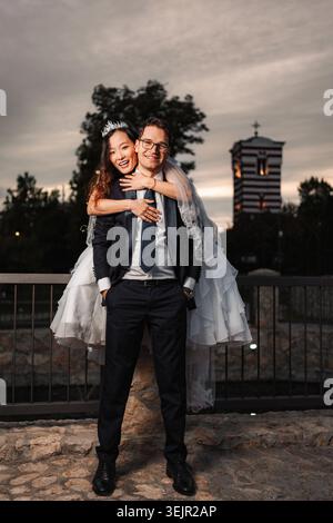 Felice coppia di sposi interrazziali che fa un giro in piggyback all'aperto Foto Stock