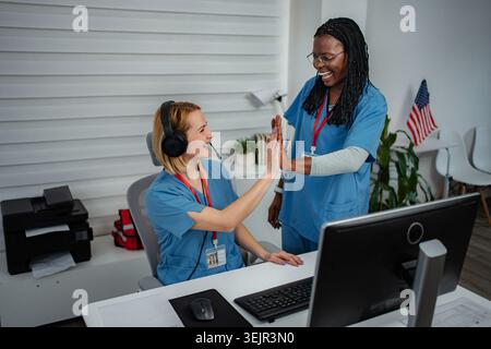 Due donne professionisti del settore sanitario che lavorano ad una scrivania in uno studio medico Foto Stock