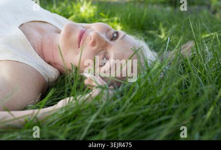 Donna anziana con lunghi capelli grigi distesi sull'erba in un parco. Foto Stock