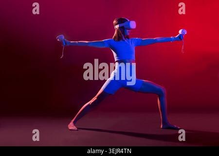 La donna pratica yoga con il visore VR, gli occhiali con tecnologia moderna con luce al neon su sfondo colorato Foto Stock