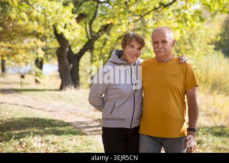 Una coppia di anziani felice guarda la fotocamera che posa e si abbraccia a vicenda in una calda giornata autunnale. copia spazio. Foto Stock