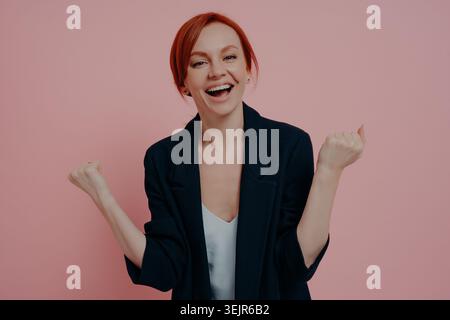 Eccitata donna d'affari dello zenzero felice isolata su sfondo rosa urlando con gioia Foto Stock