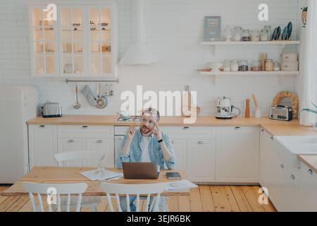 Giovane lavoratore in ufficio che lavora a distanza da casa con il computer mentre è seduto al tavolo da cucina Foto Stock