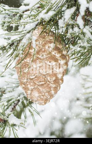 Giocattolo natalizio come cono dorato sul ramo di pino coperto di neve. All'aperto. Foto Stock