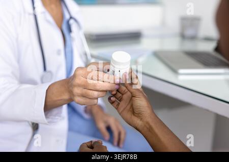 Medico donna maturo che dà una bottiglia di plastica di pillole al paziente Foto Stock